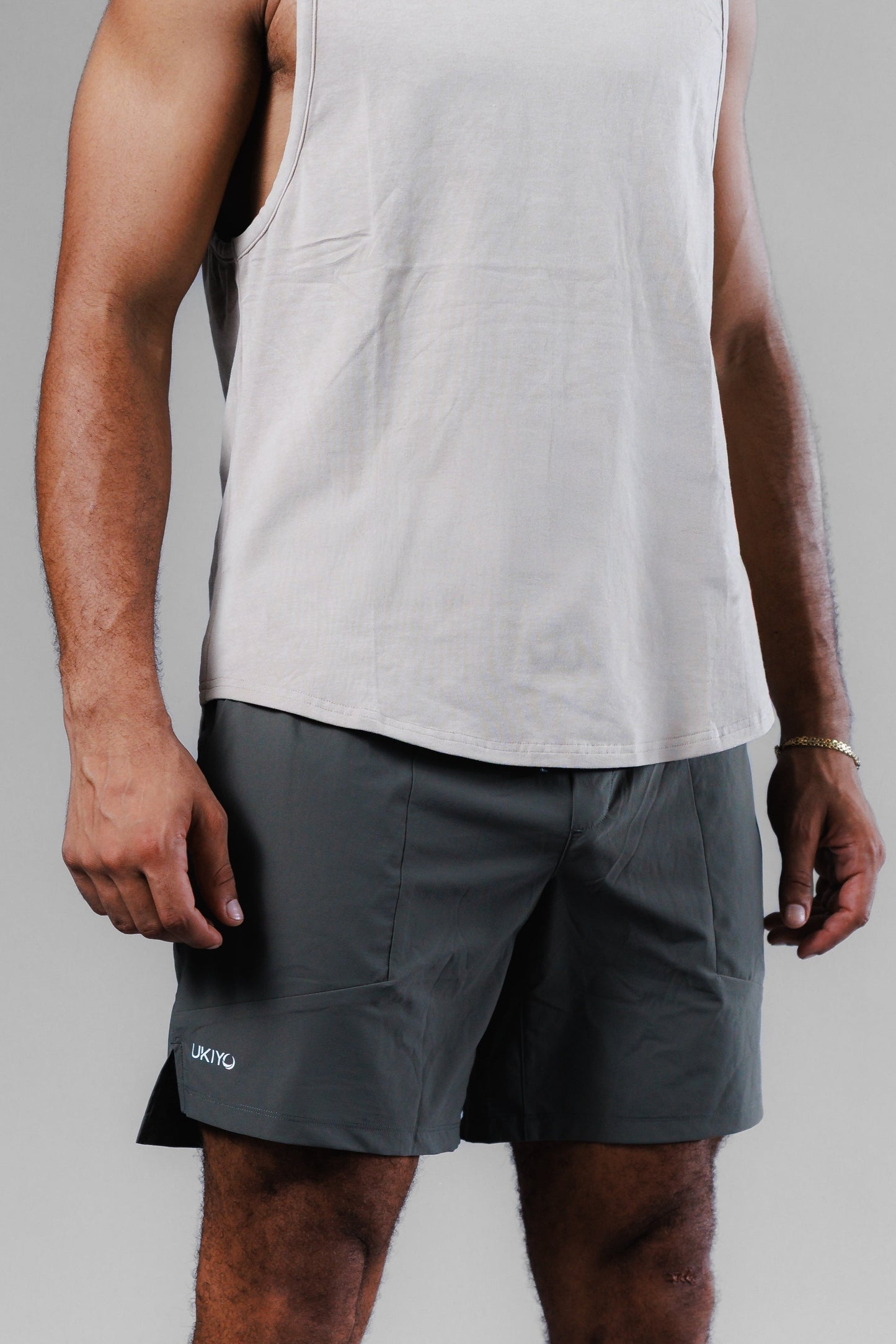 Person wearing a light gray tank top and dark gray shorts on a plain background