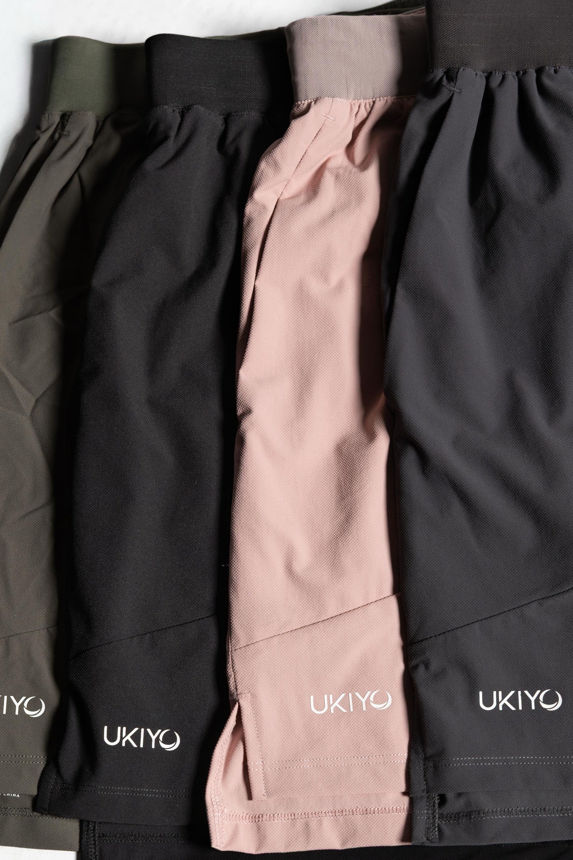Three pairs of shorts in black, pink, and gray with 'UKIYO' branding on a light gray background.