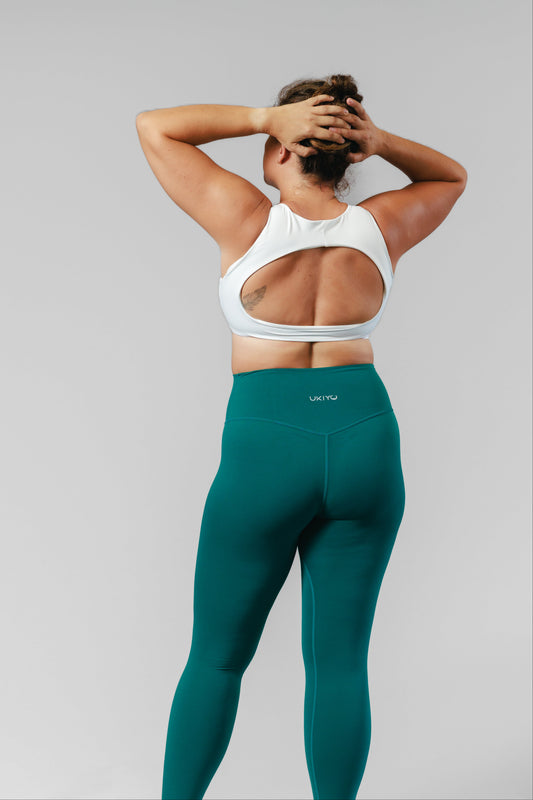 Person wearing a white sports bra and teal leggings on a gray background